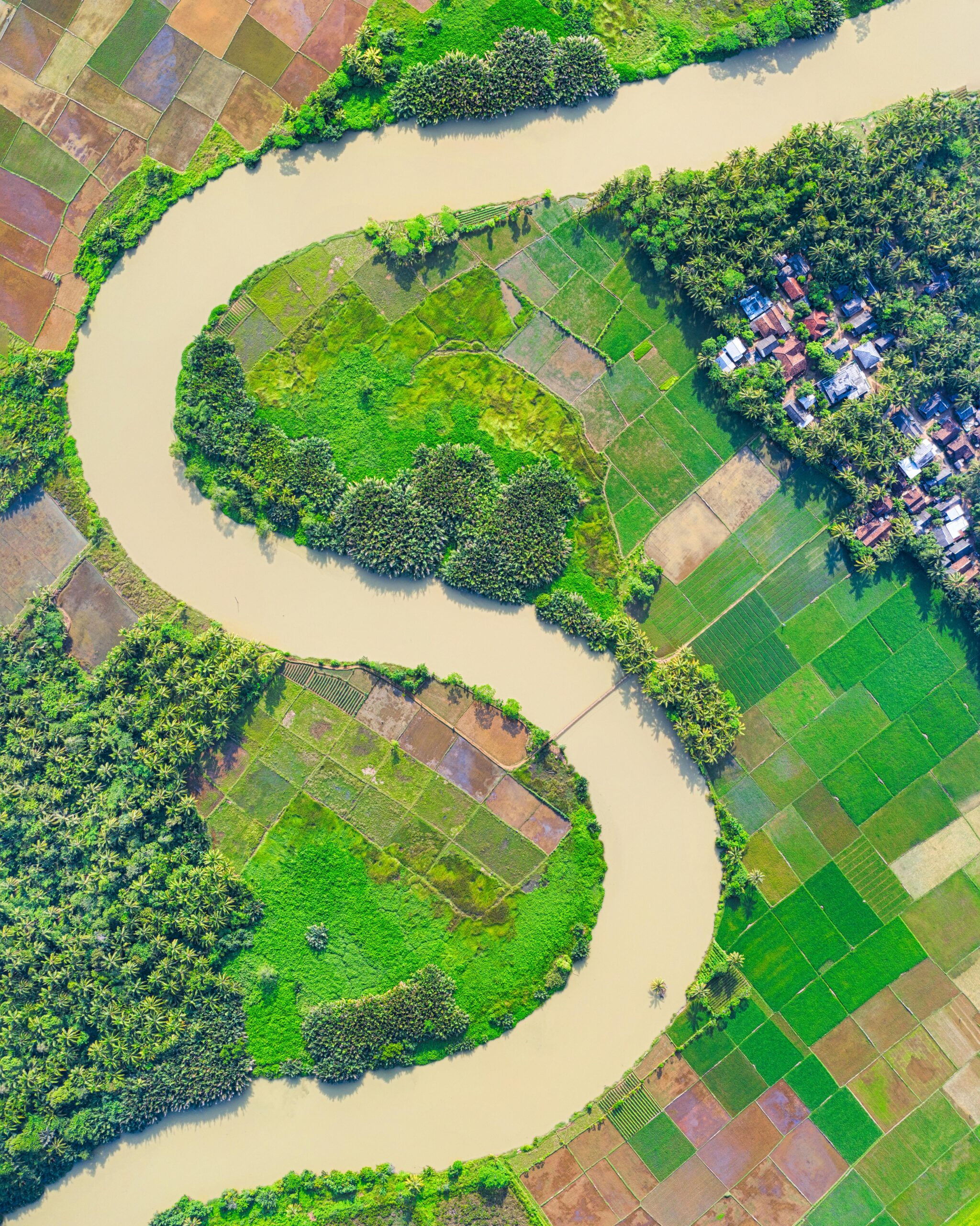 Aerial view of lush riverside farmlands in Labuhan, Indonesia, showcasing winding river bends and verdant fields.